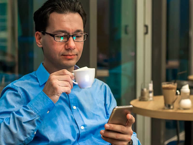 Empresário tomando café e usando o GPortal no celular
